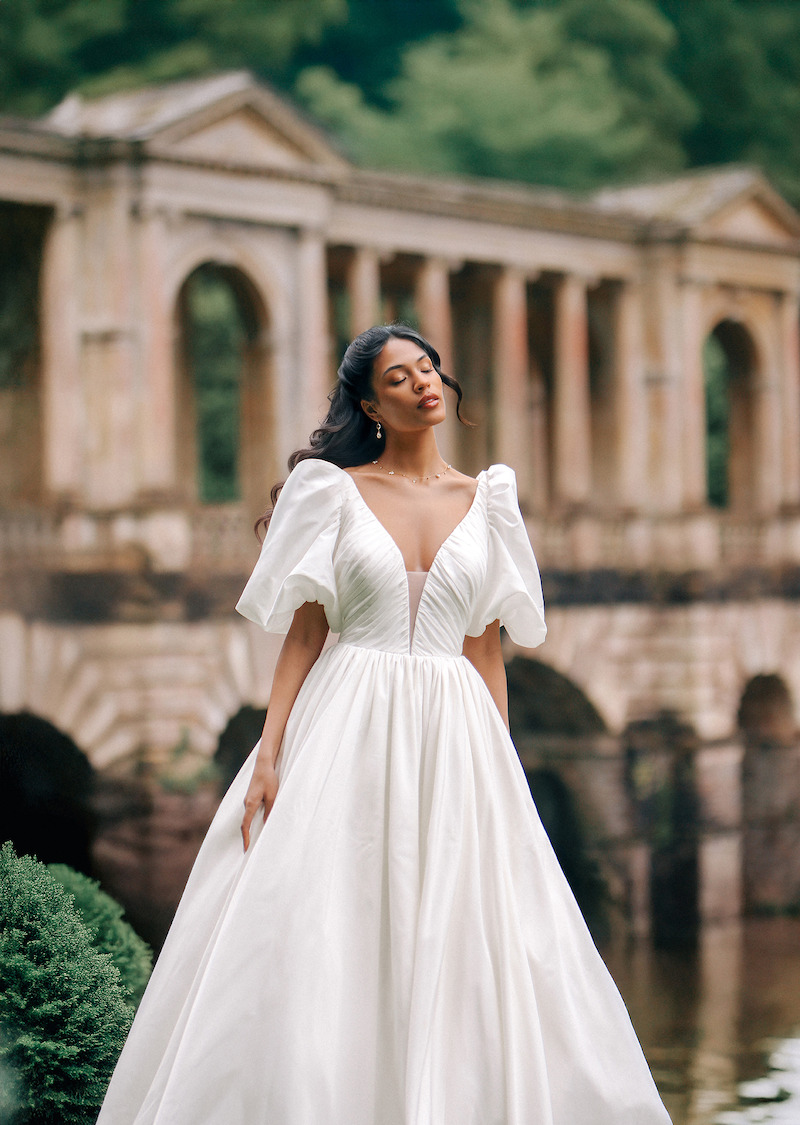 Woman in sleeved wedding dress smiles into the distance.