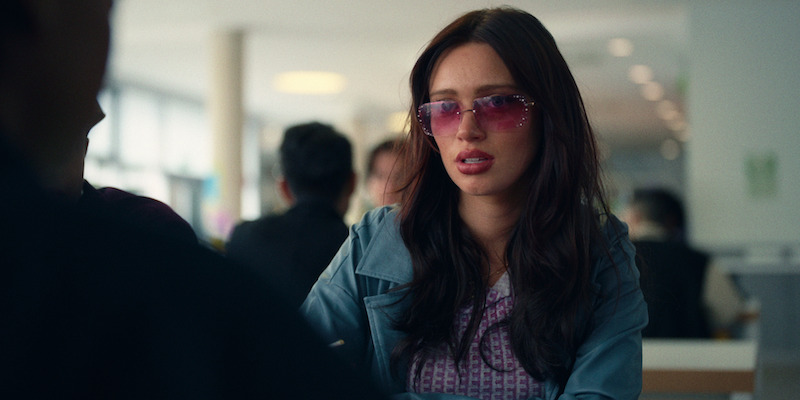 Niamh McCormack as Alison wears red tinted glasses and sits at a cafeteria table in Season 1 of 'Everything Now.'