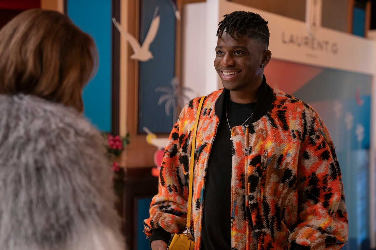 Samuel Arnold as Julien wears a bright orange jacket in Season 4 of ‘Emily in Paris.’