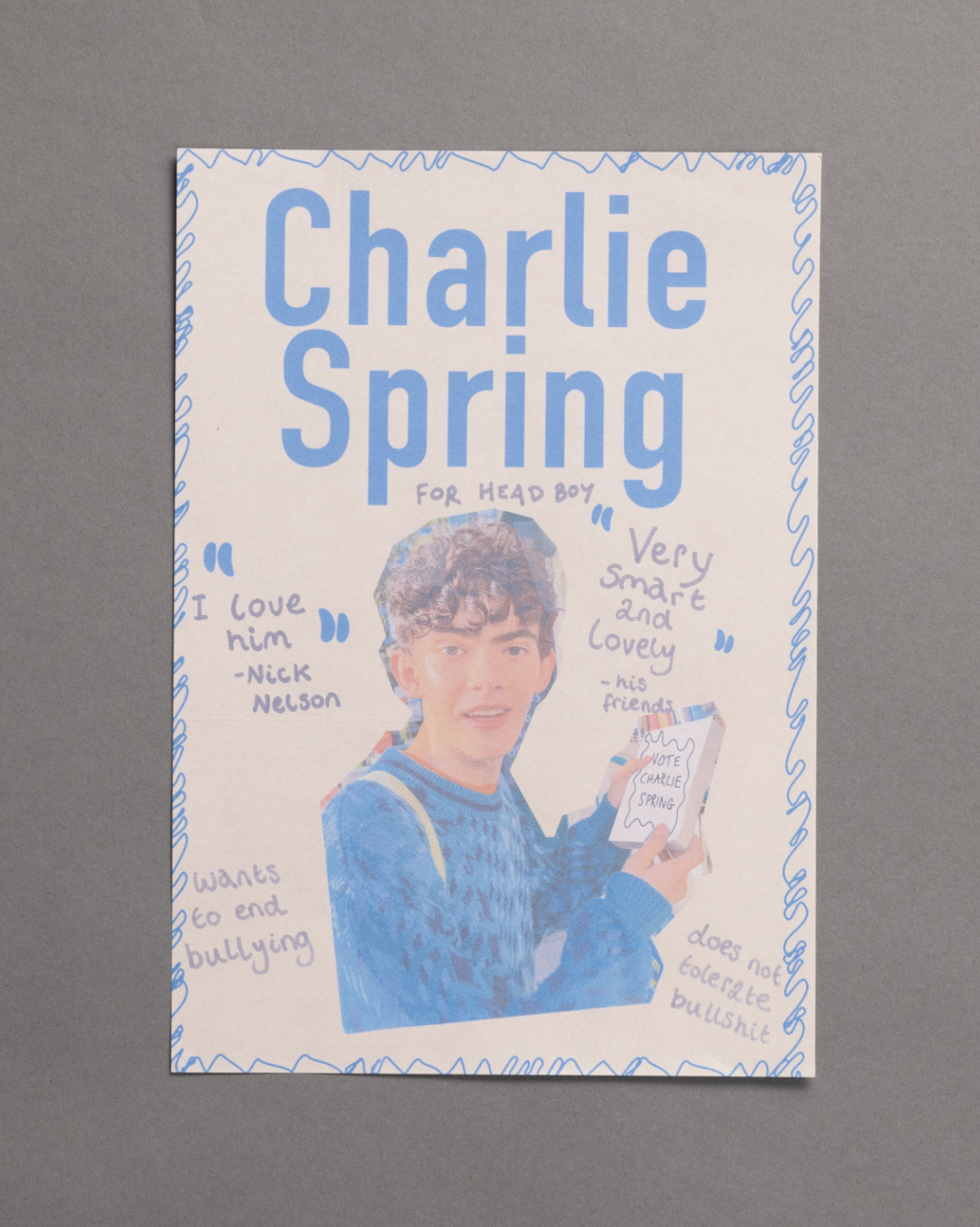 A campaign poster for Charlie Spring running for head boy, featuring a drawing of a boy in a blue sweater holding a clipboard, surrounded by positive quotes and doodles, against a gray background.