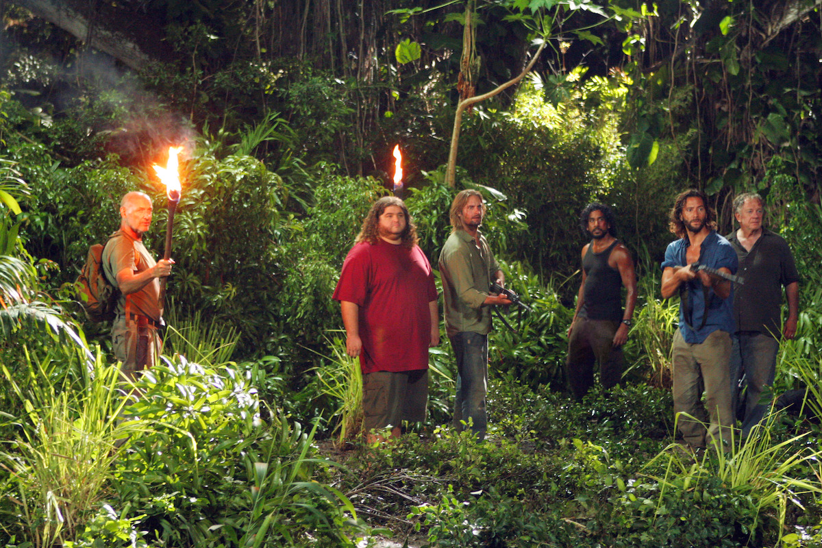 Terry O'quinn, Jorge Garcia, Josh Holloway, Naveen Andrews, Henry Ian Cusick, and Sam Anderson standing in the jungle.