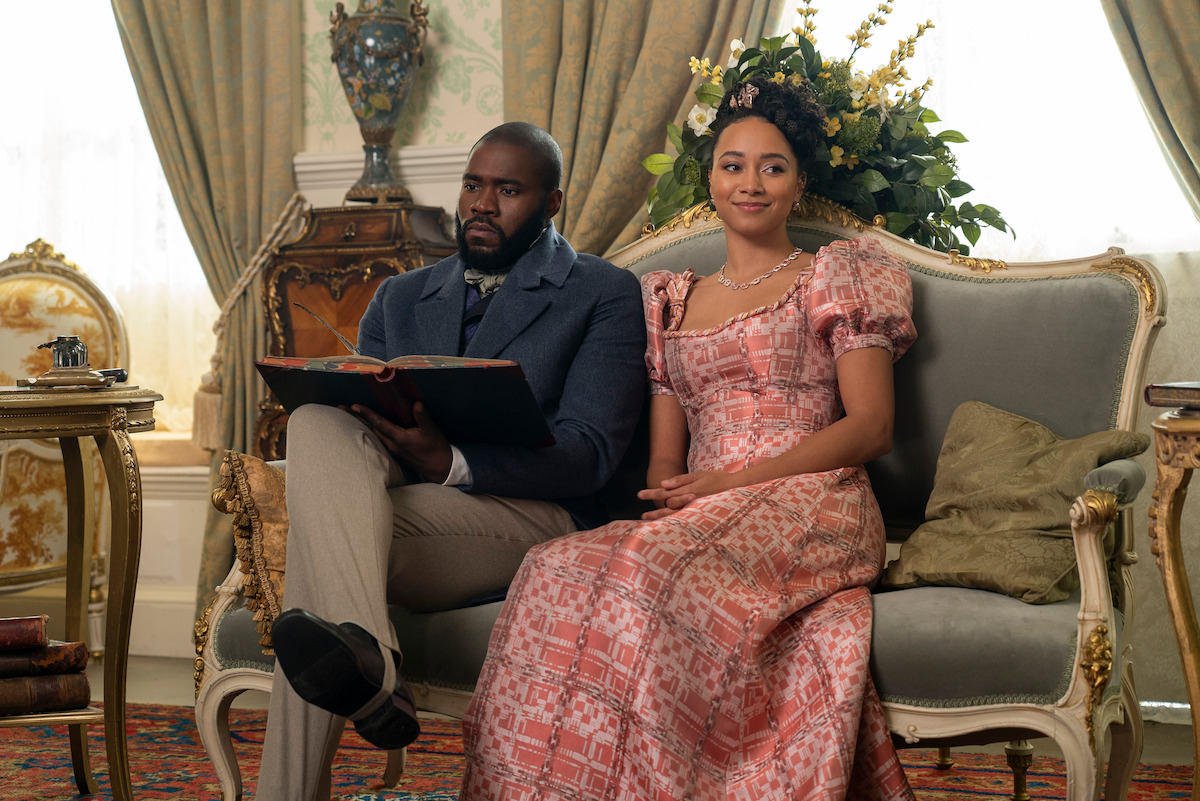 Martins Imhangbe as Will Mondrich and Emma Naomi as Alice Mondrich relax on a sofa together in Season 3 of ‘Bridgerton.’