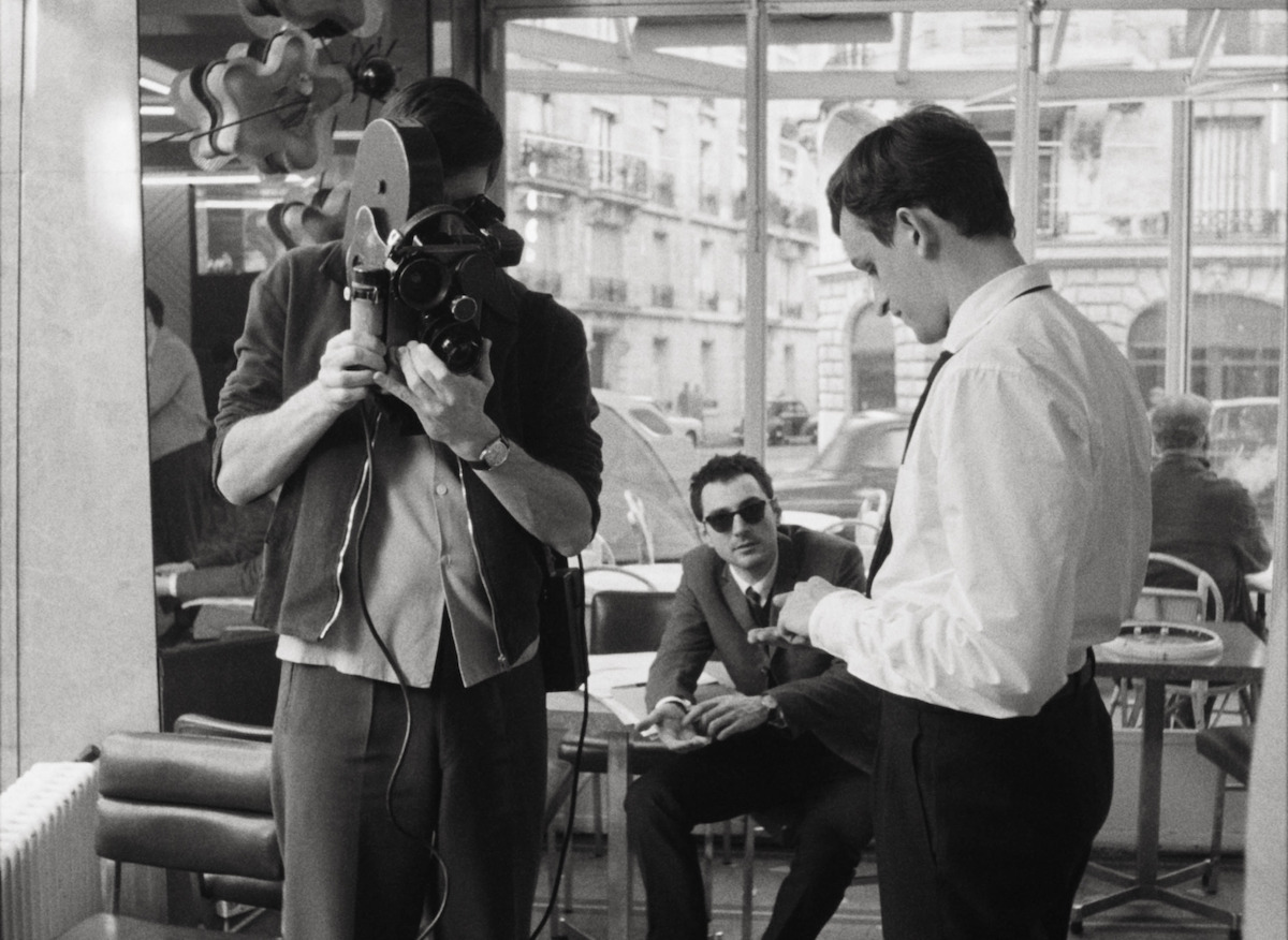 A man holds an old fashion film camera pointed at Belmondo played by Aubry Dullin