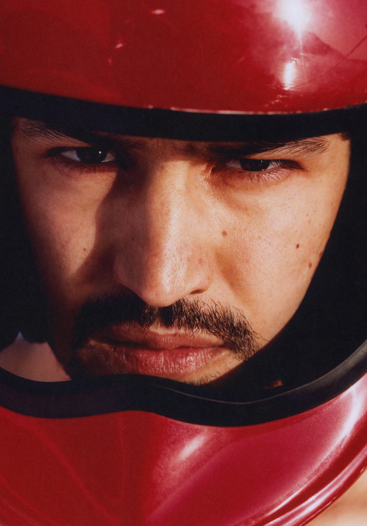 Gabriel Leone wears a red helmet and looks angsty on a beach.