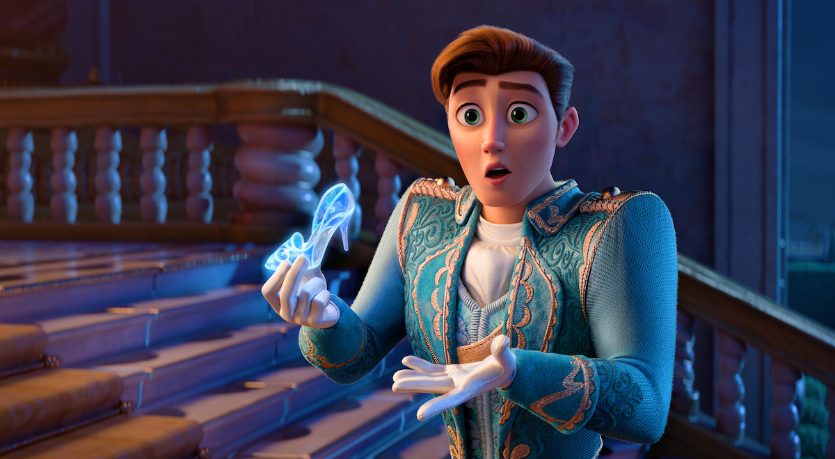Animated prince in ornate blue suit stands on palace staircase, looking surprised as he holds a glowing glass slipper, with elegant railing and night sky visible in the background.