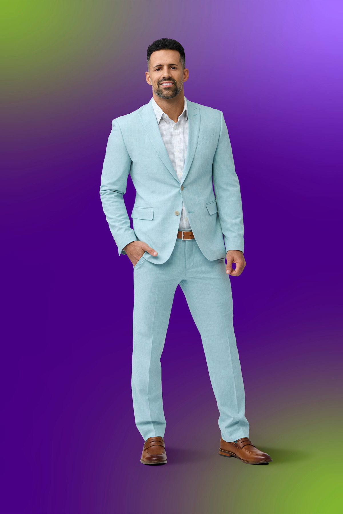Man in a light blue suit and brown shoes standing confidently against a vibrant purple and green gradient background, posing with one hand in his pocket.