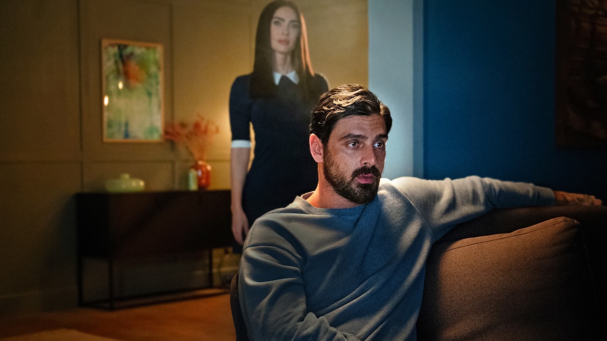 In an image from the movie ‘Subservience,’ Megan Fox as Alice stands behind Michele Morrone as Nick, who sits on a couch.