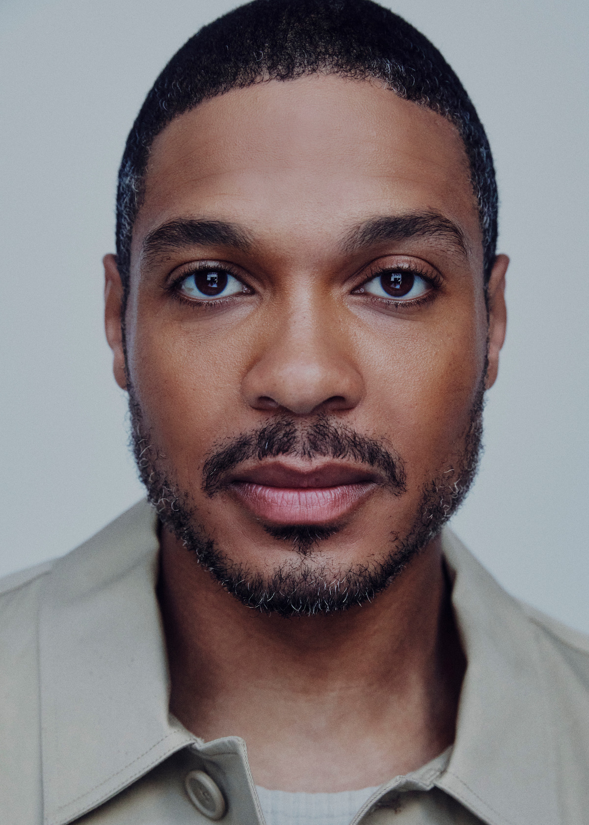 Ray Fisher wears a tan jacket and stares at the camera.