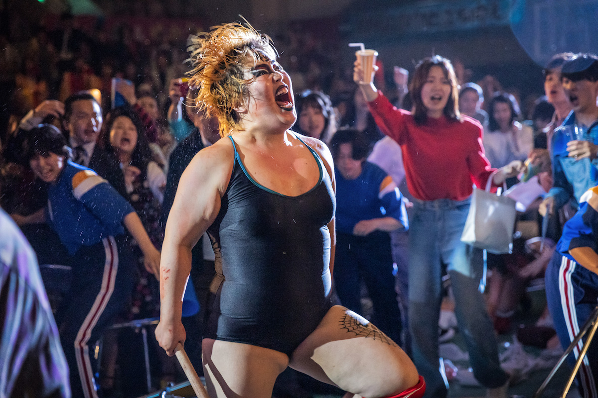 Yuriyan Retriever as Kaoru “Dump” Matsumoto yells at a wrestling arena in Season 1 of ‘The Queen of Villains.’
