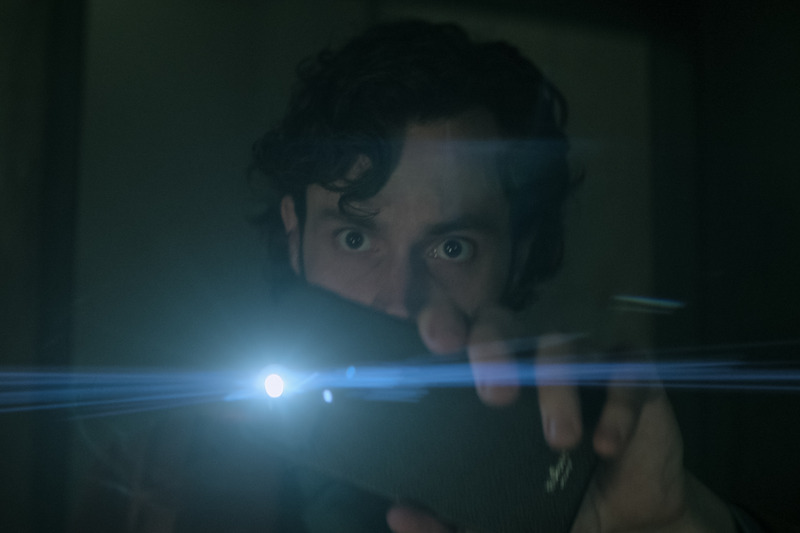 Badgley as Joe Goldberg holding a cellphone. 