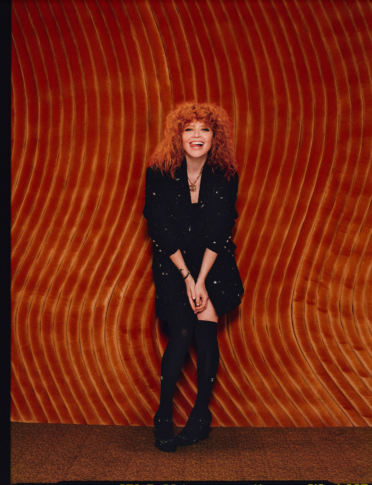 Natasha Lyonne poses against a red background wearing a sequined ensemble.