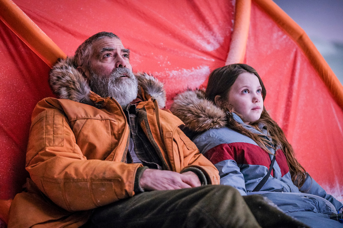 An older man and young girl lean against a tent with snow on it