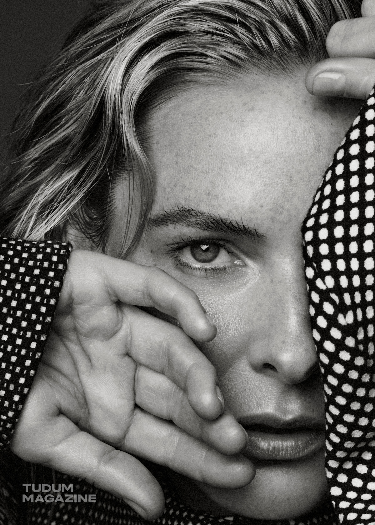 Rebecca Ferguson, wearing a polka-dot blouse, covers her face with her hands.