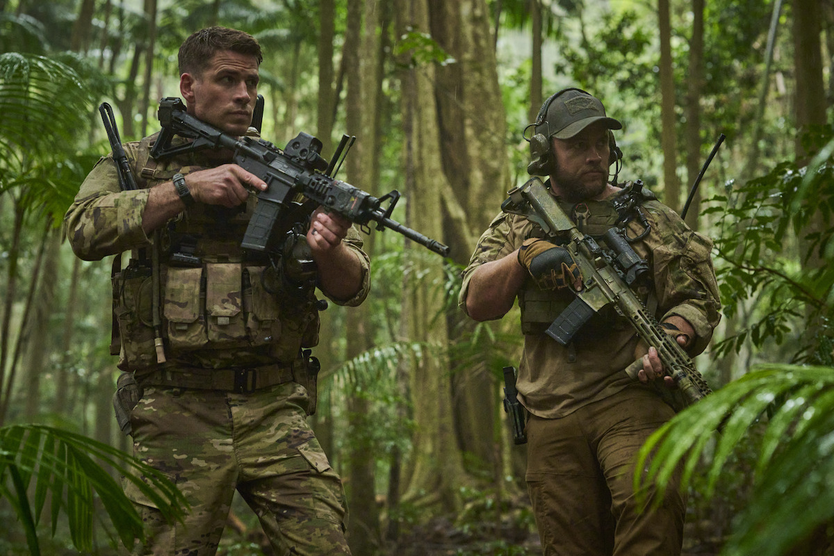 Liam Hemsworth as Sergeant JJ Kinney and Luke Hemsworth as Sergeant Abell walk through a jungle holding guns in an image from the film ‘Land of Bad.’