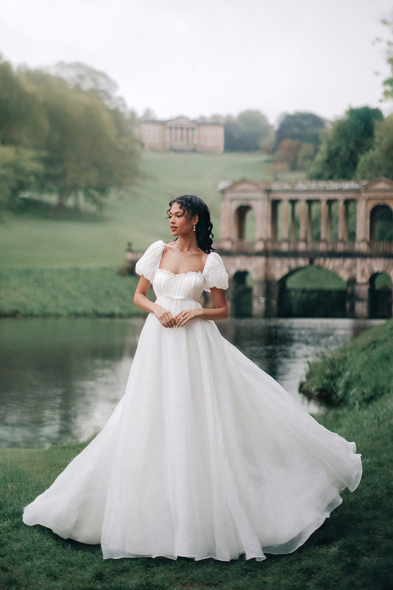 Woman in bridal dresses poses and looks off into the distance.