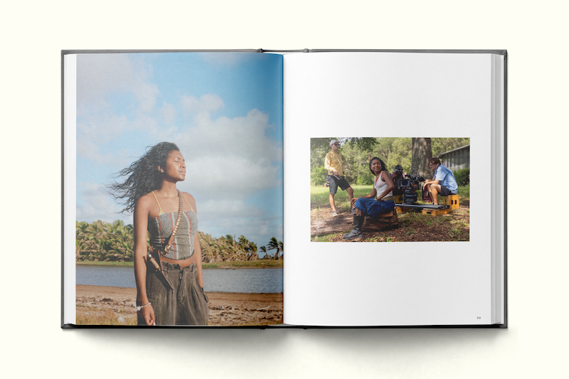 Open photo book showing a woman standing by water with trees and blue sky, while the opposite page features three people in a shaded outdoor setting with greenery and film equipment.