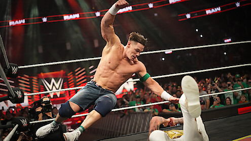 A wrestling match in a packed arena with a muscular wrestler mid-air attacking an opponent on the mat, energetic crowd cheering, bright lights, intense and action-packed atmosphere.