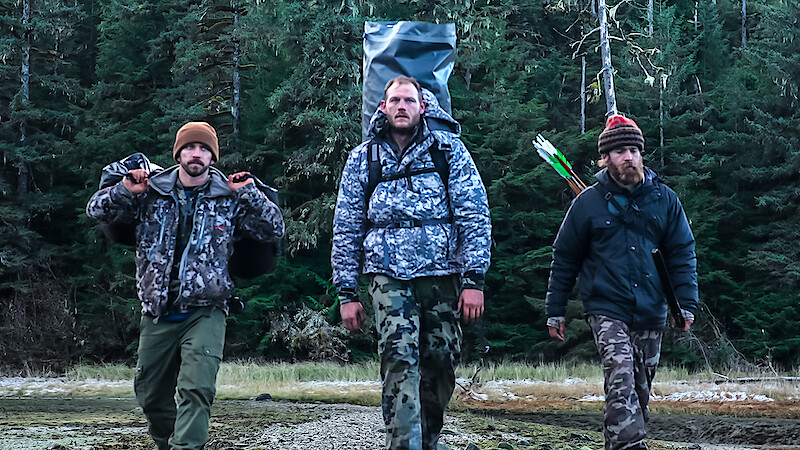 Three 'Outlast' Season 2 contestants walk towards the camera with their equipment and supplies.