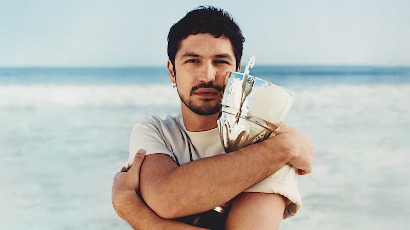 Gabriel Leone wears a white t-shirt and clutches a trophy to his chest.