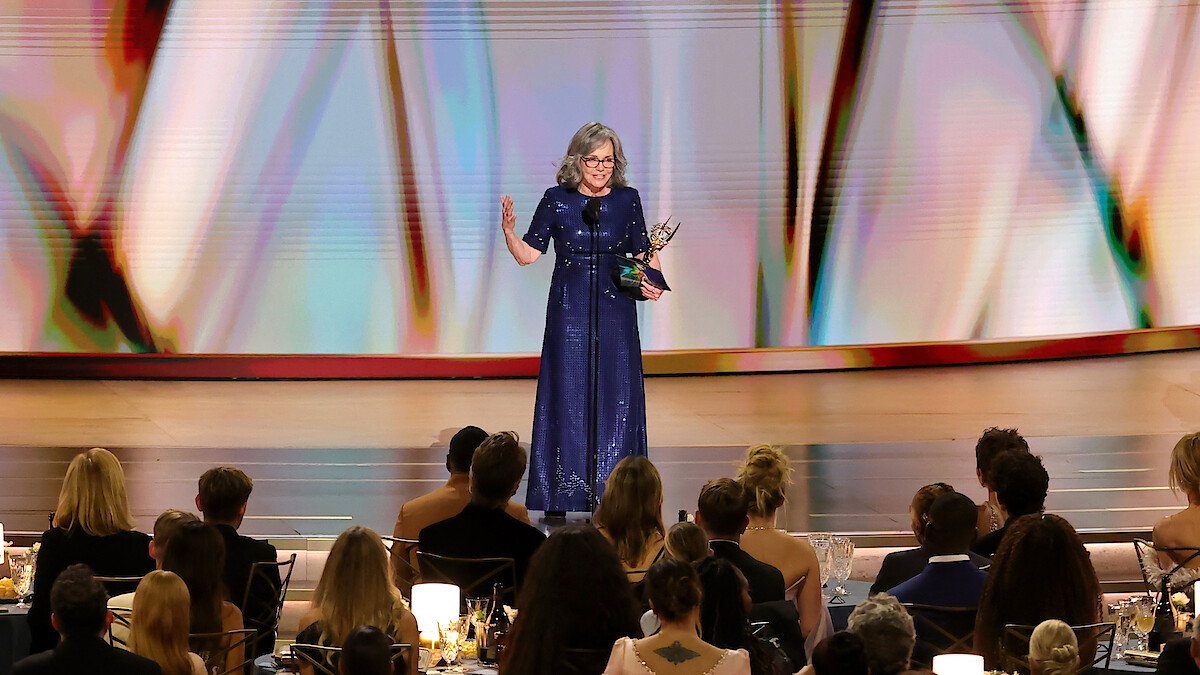 Uma mulher usando um vestido azul aparece no centro do palco recebendo uma premiação no Emmy 2026