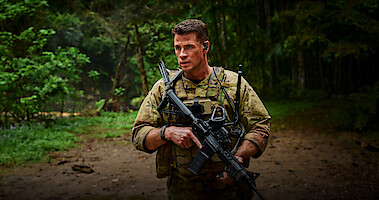 Liam Hemsworth as Sgt. JJ Kinney walks through a jungle holding a gun in 'Land of Bad'