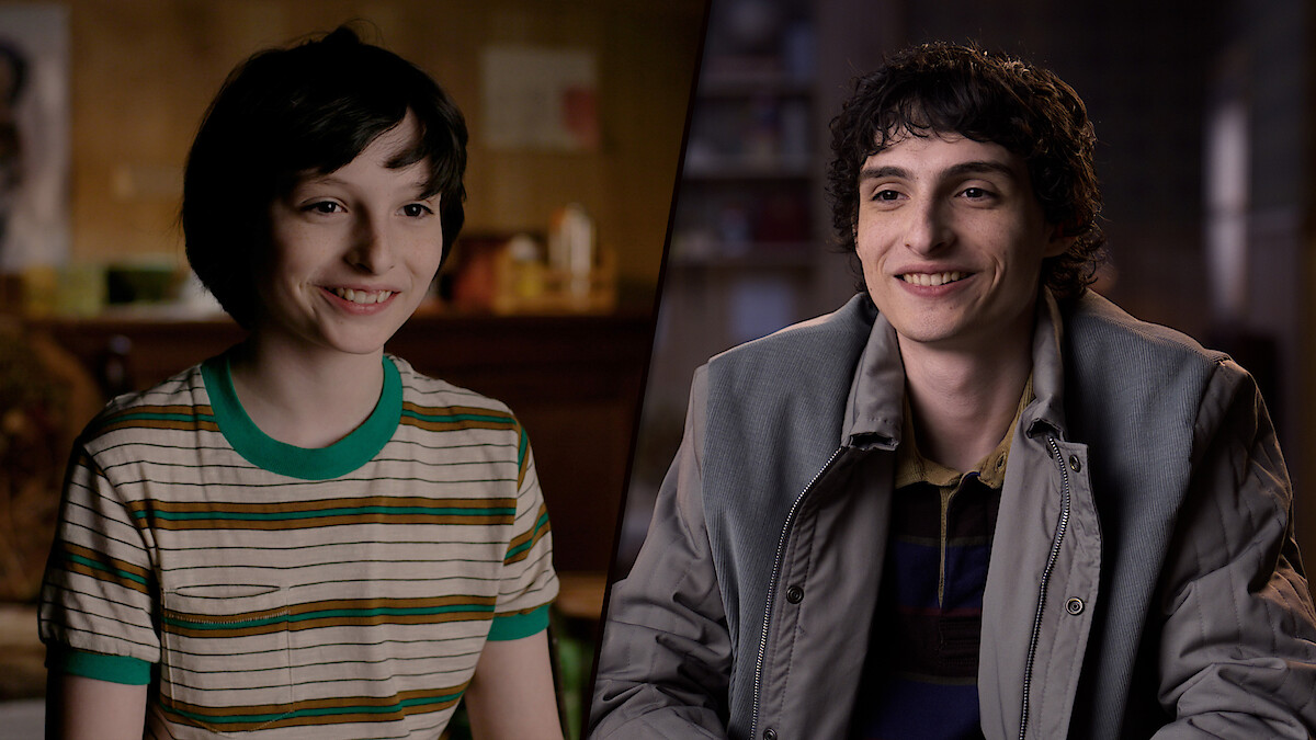 Side-by-side images of Finn Wolfhard at different ages; on the left, he wears a striped shirt in a cozy room, and on the right, he’s older, wearing a jacket, sitting in a warmly lit indoor setting.