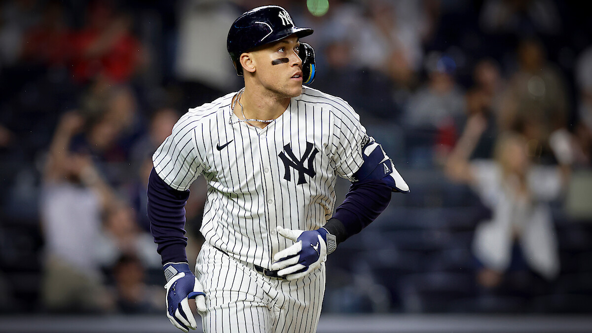 New York Yankees baseball player in pinstripe uniform runs on field during a night game; blurred crowd in the background creates an energetic, competitive atmosphere.