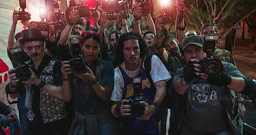 Robbie Tann as XX, Zazie Beetz as XX, Danny Ramirez as XX, and James Rees as XX stand holding cameras in a crowd of paparazzi in Season 6 of Black Mirror.