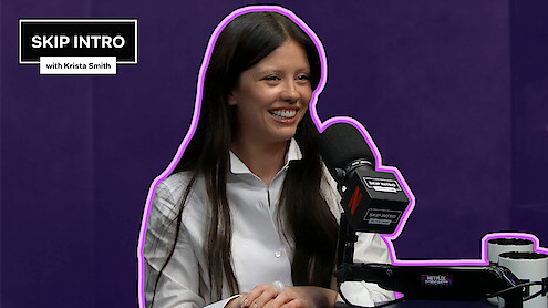 Mia Goth sits smiling in front of a microphone during a podcast recording for "Skip Intro with Krista Smith." The background is purple, and the podcast logo appears in the top left corner.