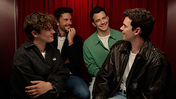Will Tilston, Jonathan Bailey, Luke Thompson, and Luke Newton sit in a photo booth with red curtains. 