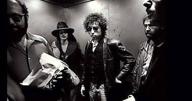 Bob Dylan stands in an elevator surrounded by other people in 'Rolling Thunder Revue: A Bob Dylan Story by Martin Scorsese.'