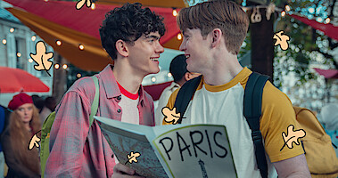 Joe Locke as Charlie and Kit Connor as Nick smiling together on the streets of Paris in Season 2 of Heartstopper. 
