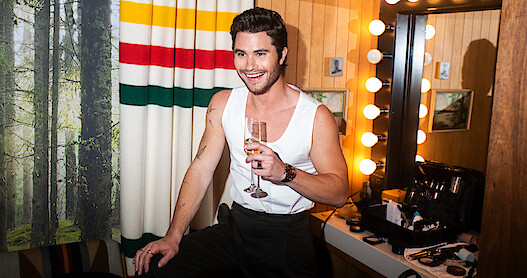 Chase Stokes in dressing room holding champagne.