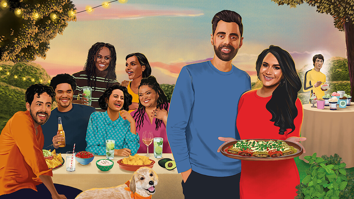 A group of people enjoying an outdoor dinner party with drinks and food, set in a garden with string lights. A couple stands in the front holding a large dish, while a dog sits beside them and more food is on a table in the background.