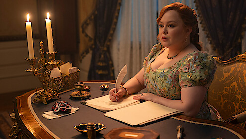 Woman in a floral dress writes with a quill at an ornate wooden desk with candles, in a lavish, candlelit room with elegant curtains and antique decor.