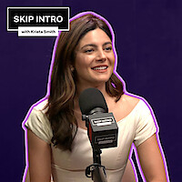 Monica Barbaro smiles in front of a microphone, framed by a deep purple background with a matching purple outline surrounding her.