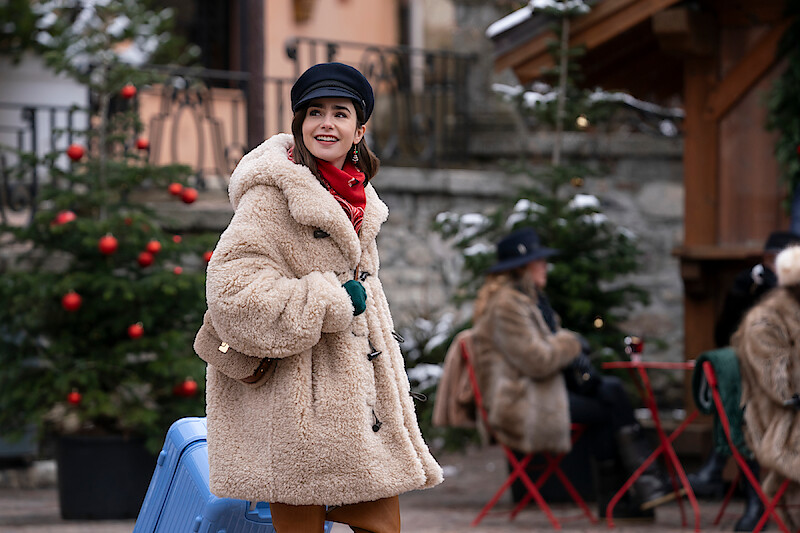 Lily Collins, como Emily, caminha por uma feira de árvores de Natal na temporada 4 de ‘Emily em Paris’