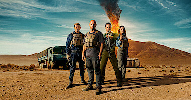 The cast of 'Wages of Fear' stands in front of an explosion 