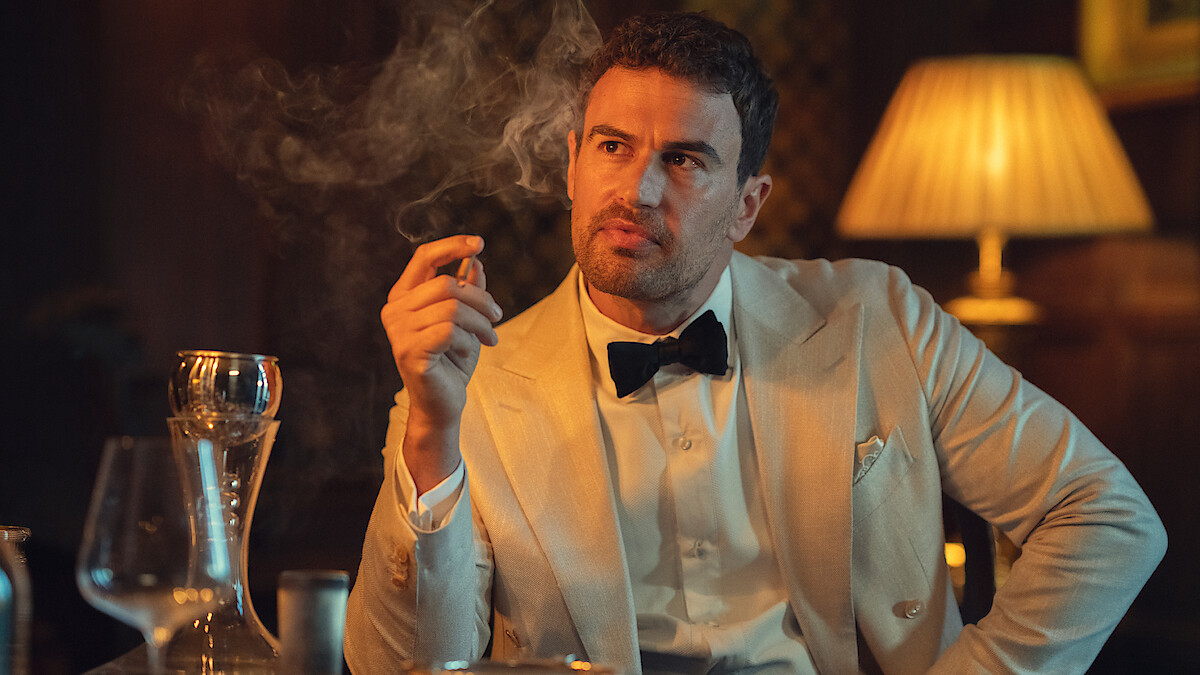 Man in a white tuxedo jacket and black bowtie sits at a dimly lit table holding a cigar, surrounded by wine glasses, a decanter, and a glowing lamp, with smoke swirling in the moody atmosphere.