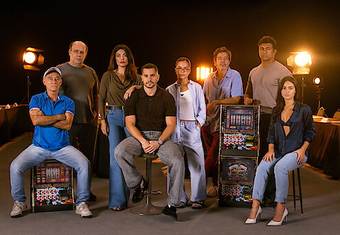 Elenco principal da série "Donos do Jogo" posa ao lado de máquinas caça-níquel