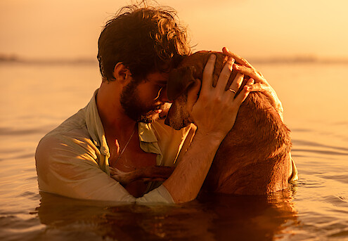 Homem (Rafa Vitti) e cachorro se abraçam em uma cena no mar do filme 'Caramelo'
