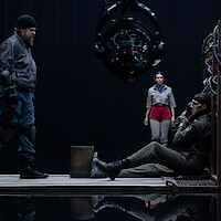 A tense film set scene with three actors and a large camera rig.