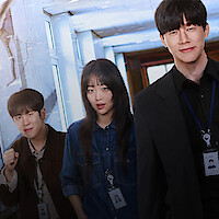 Four people wearing work ID badges stand in a well-lit hallway, dressed in business and casual attire, suggesting an office or professional environment.