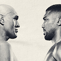 Two male boxers face each other in a staredown against a plain light background, highlighting intensity and anticipation in a sports setting.