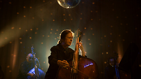 Orin O’Brien playing her double bass on stage under a mirrorball