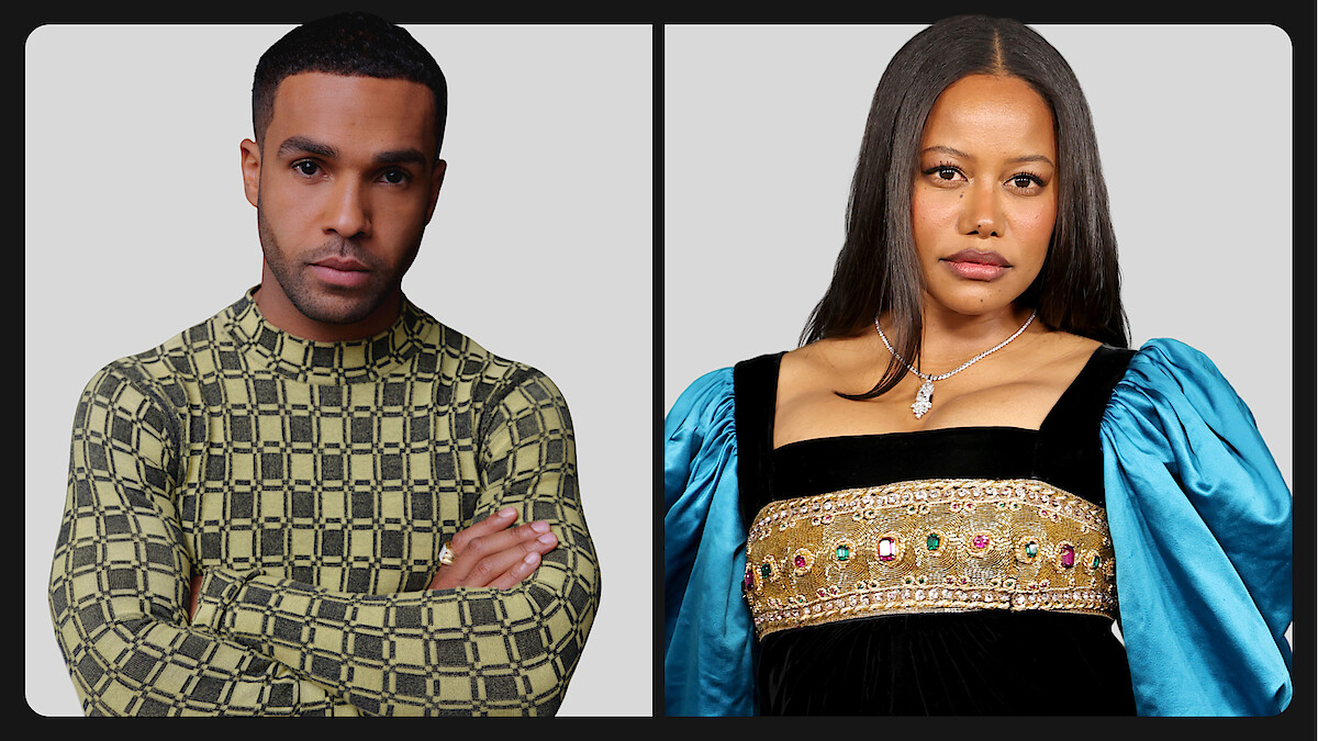 Two people posing against a plain gray background; the person on the left wears a patterned long-sleeve shirt, arms crossed, while the person on the right wears a dress with blue puffed sleeves and decorative details.