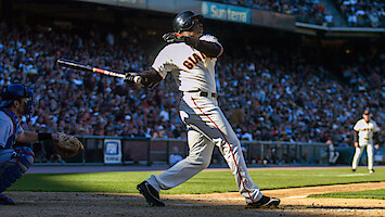 Barry Bonds in a Giants uniform swinging bat during a sunny game, catcher and umpire nearby, large crowd in stadium background.