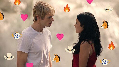 A young man and woman stand facing each other outdoors, possibly near a waterfall. Colorful icons of hearts, flames, horses, cowboy hats, and teapots are overlaid on the image, adding a playful, romantic tone.