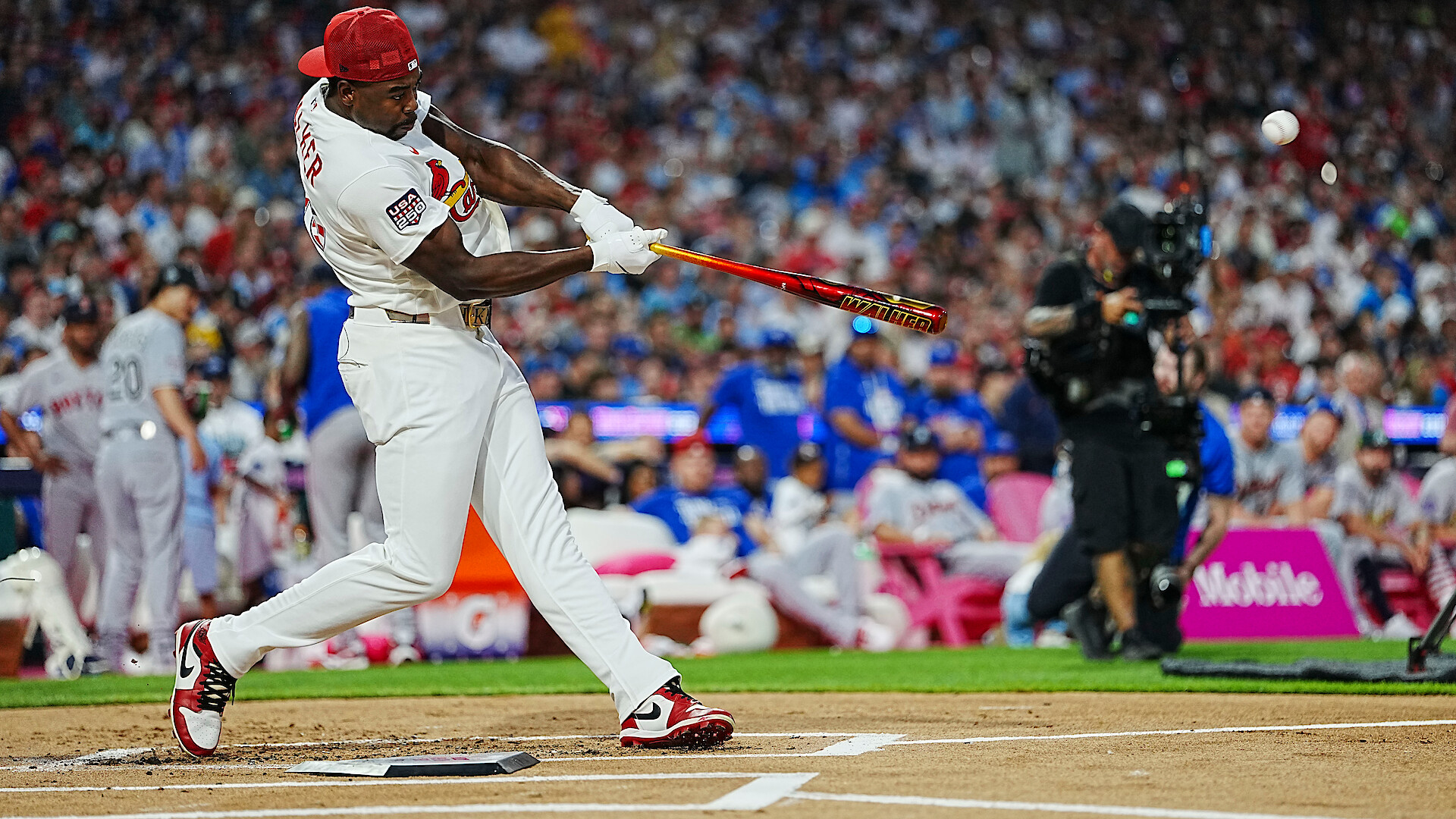 Baseball player in white uniform swinging bat during a game, crowded stadium background with spectators and photographers, action shot captured at home plate.