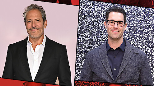 Two men in suits pose separately against different backdrops; the man on the left stands before a plain light background, while the man on the right stands in front of a patterned black and white wall. Both are smiling and appear at a formal event.